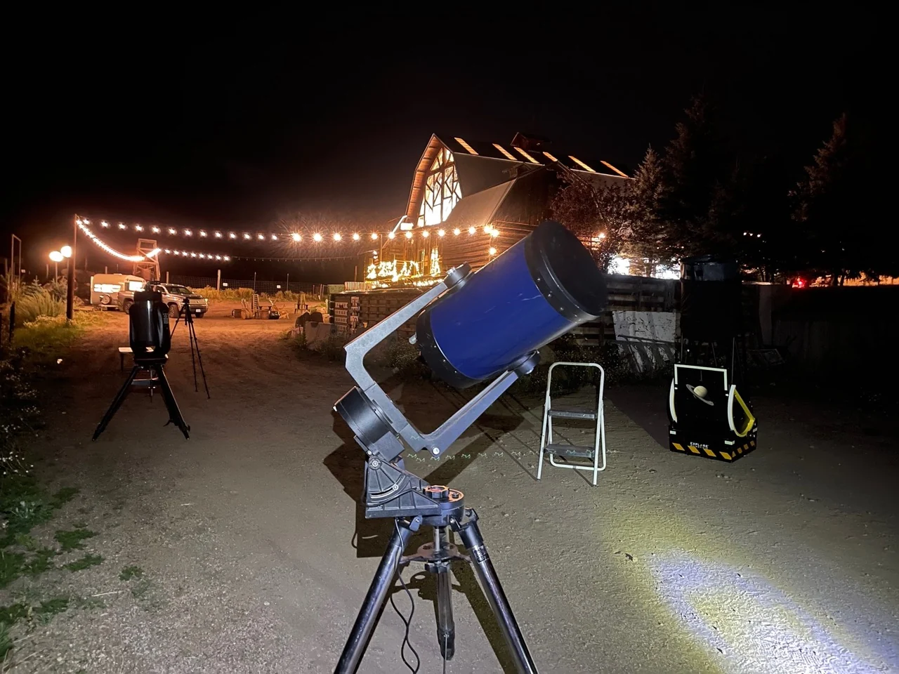 A large telescope ready for an AstroTours evening session beside a warmly lit building